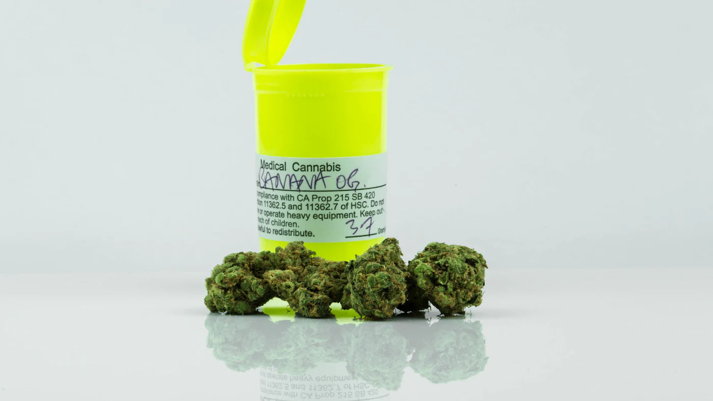 A medical cannabis container with a handwritten label beside cannabis buds