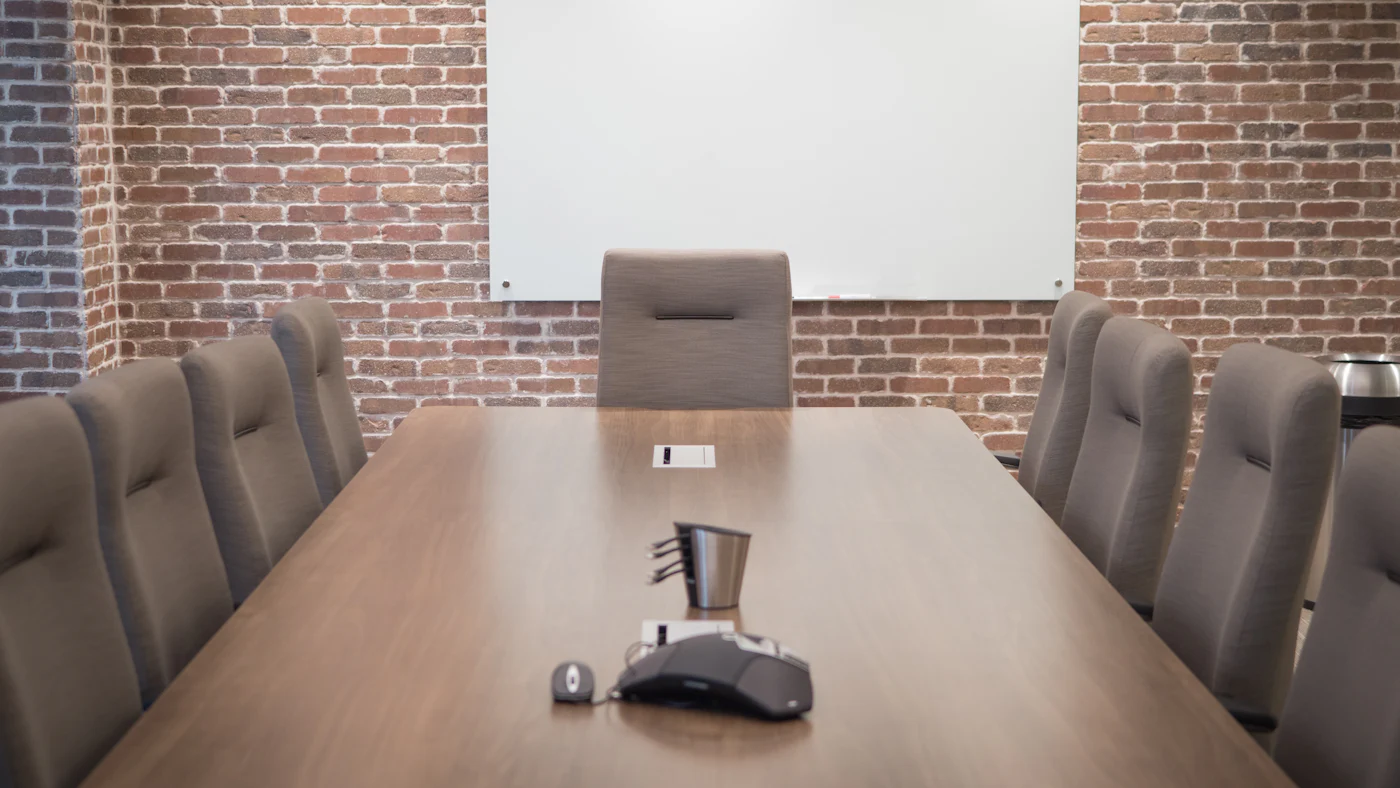 An empty conference table with chairs facing a blank screen